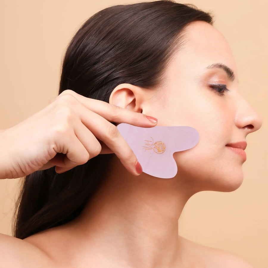 Woman using pink facial gua sha tool for skincare routine, promoting glowing healthy complexion